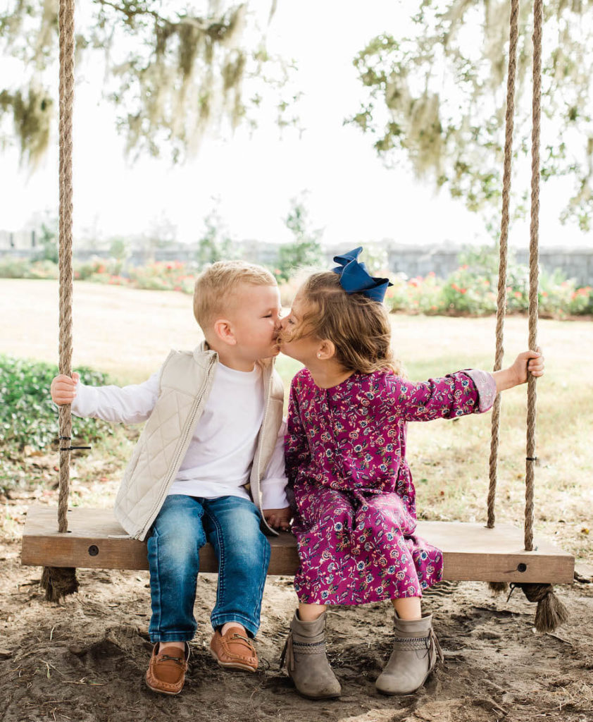 Two kids sit on a swing and kiss each other